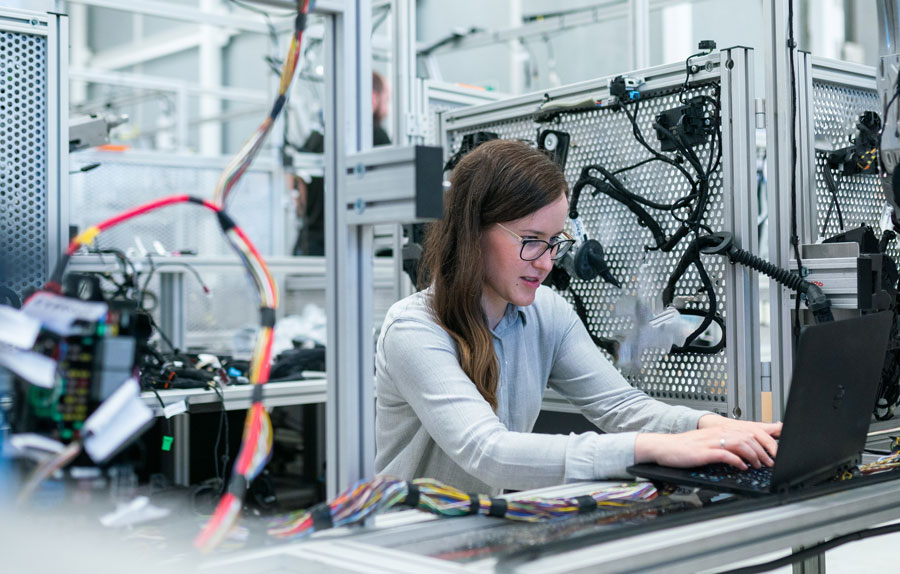 Woman working on a computer surrounded by cables in a a work-shop like a computert repair shop or electronics repair shop